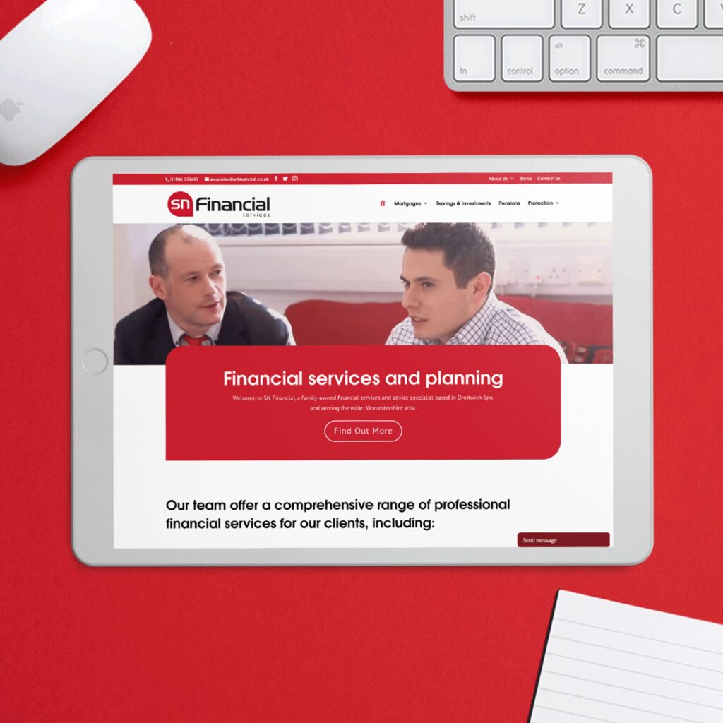 SN Financial homepage on ipad with mouse, keyboard and notebook on red background